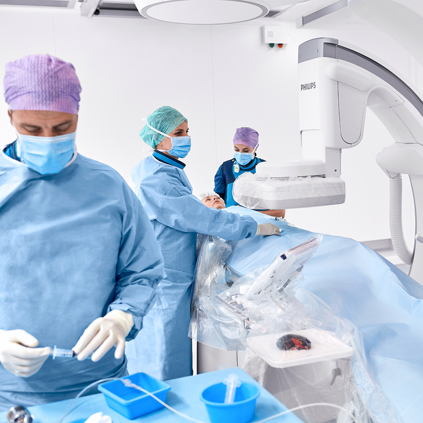 Medizinische Fachkräfte mit OP-Kleidung und Masken arbeiten an einem Patienten unter einem medizinischen Gerät.