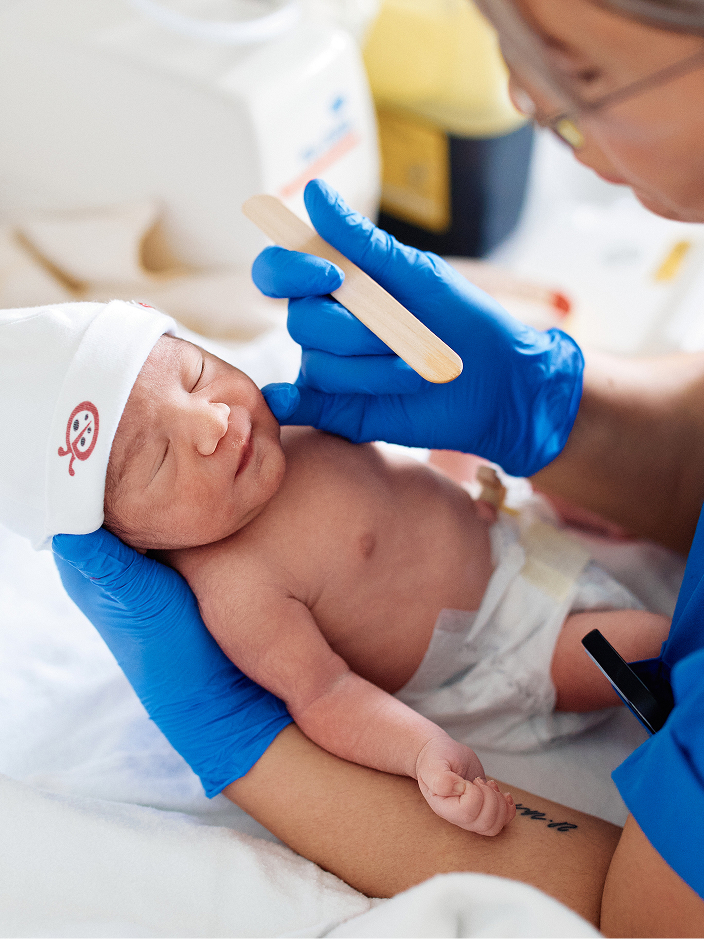 Ein Neugeborenes wird von einer Person mit blauen Handschuhen untersucht.