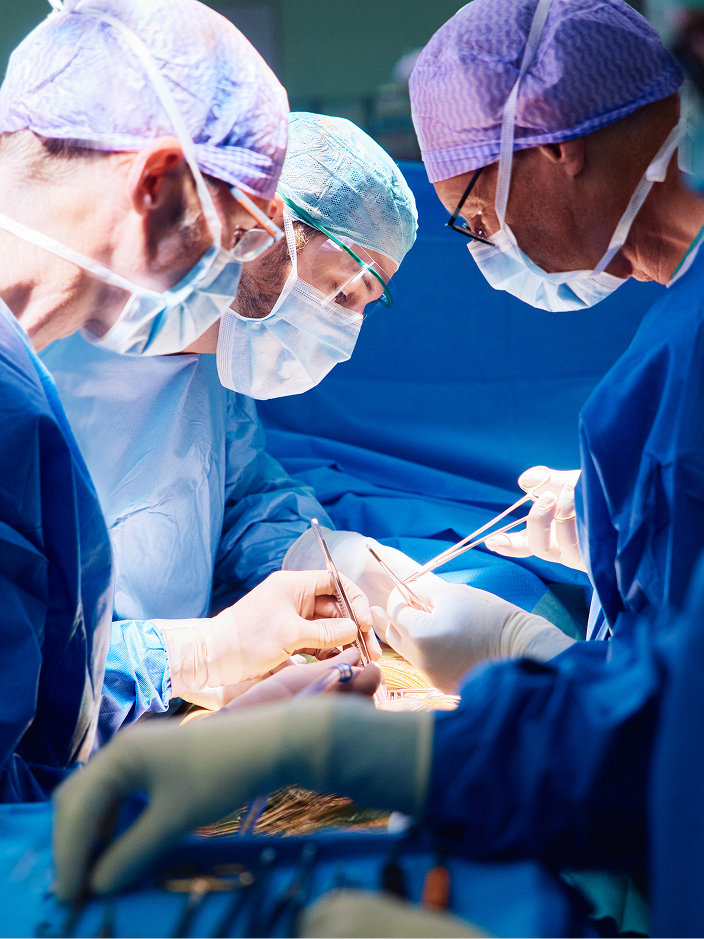 Chirurgen in OP-Kleidung führen eine Operation durch, sie schauen konzentriert auf einen Patienten, der vor ihnen auf dem OP-Tisch liegt.