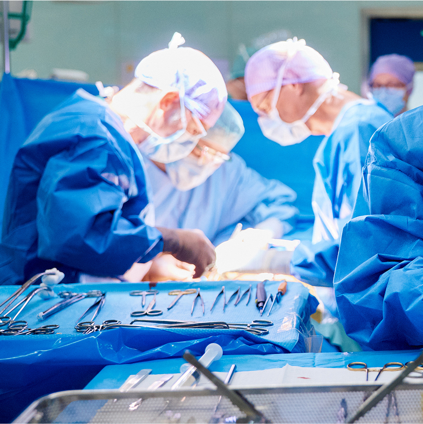 Chirurgisches Team in blauen Kitteln und Masken bei einer Operation, umgeben von Instrumenten auf einem Tisch.