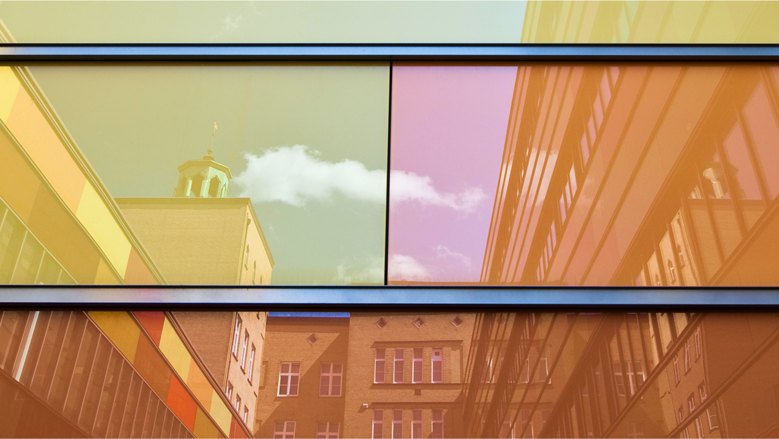 Reflektierende Fensterfassade mit bunten Farbtönen, in der sich ein Gebäude und Wolken spiegeln.