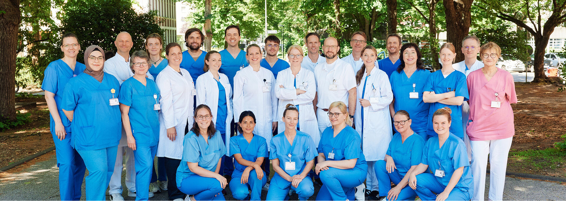 Gruppe von Personen in medizinischer Kleidung, die im Freien vor Bäumen posiert.