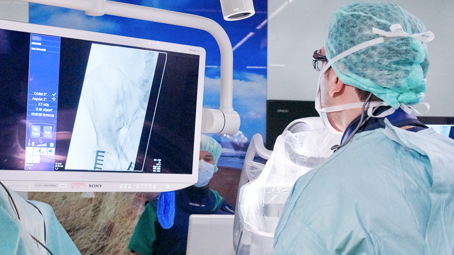 Ein Chirurg in Schutzkleidung betrachtet einen Monitor mit medizinischen Bildern in einem Operationssaal.