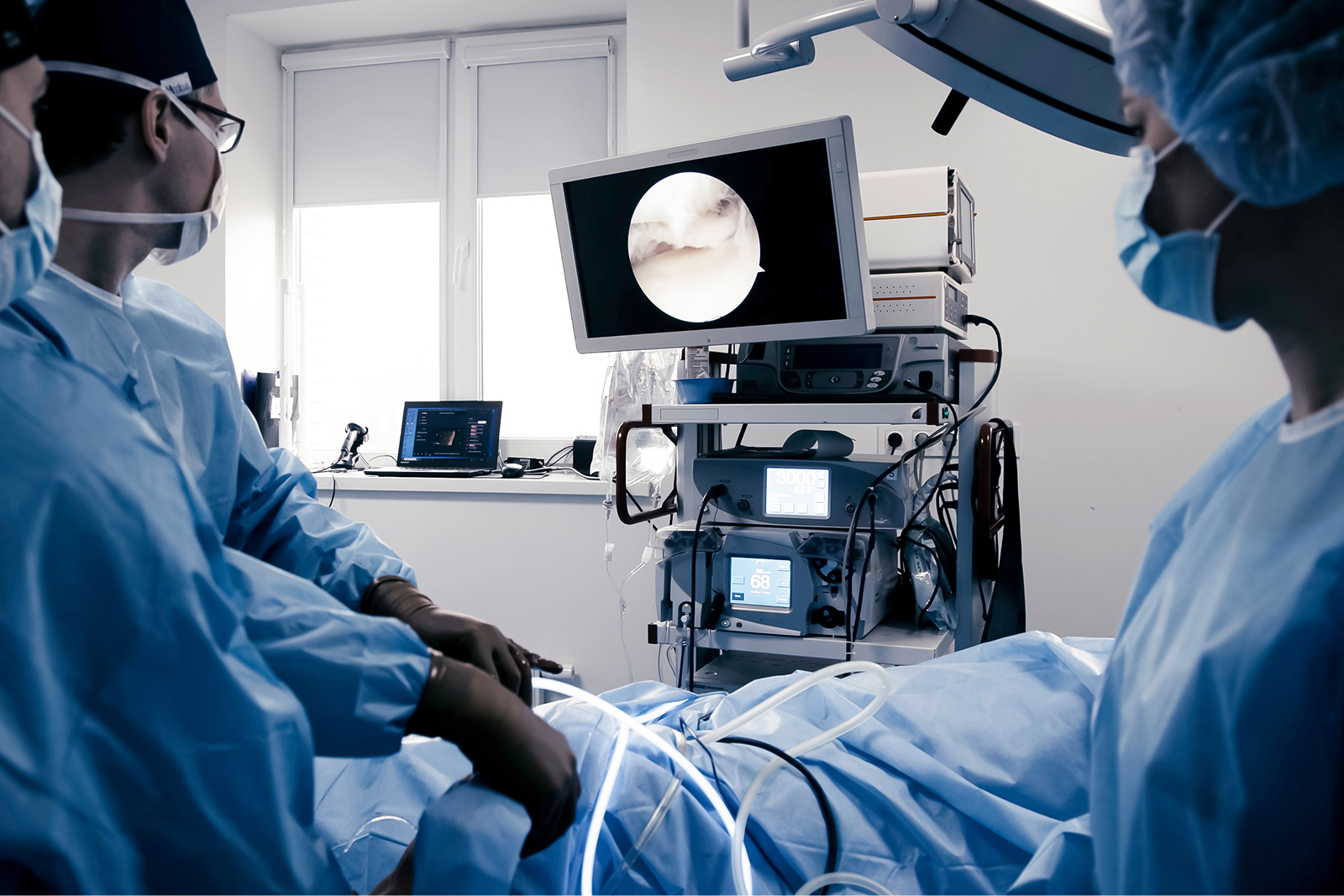 Chirurgisches Team in blauer Kleidung, das einen Patienten behandelt und dabei auf einen Monitor schaut.