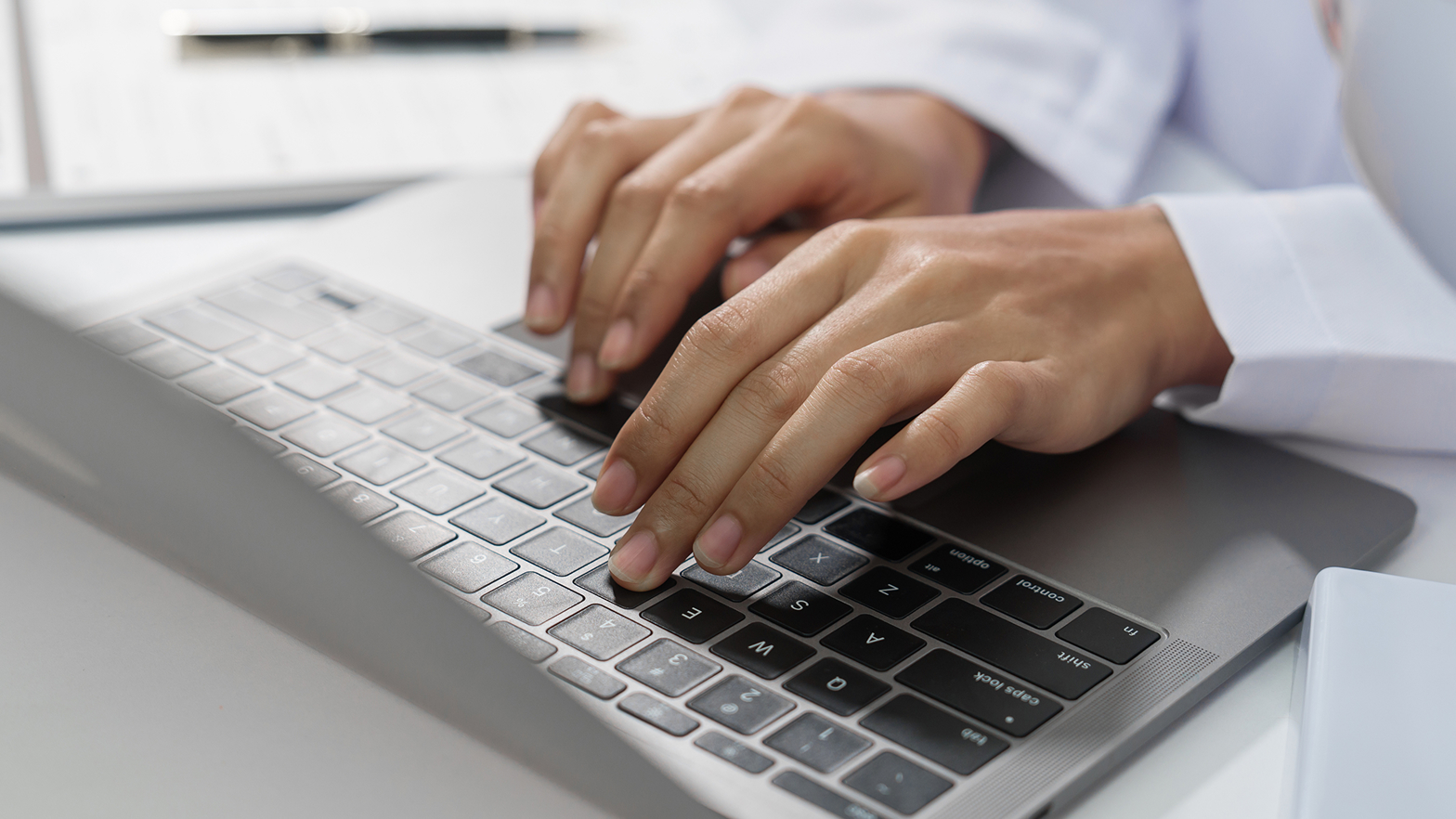 Die Hände einer medizinischen Fachkraft tippen auf einer Laptop-Tastatur.