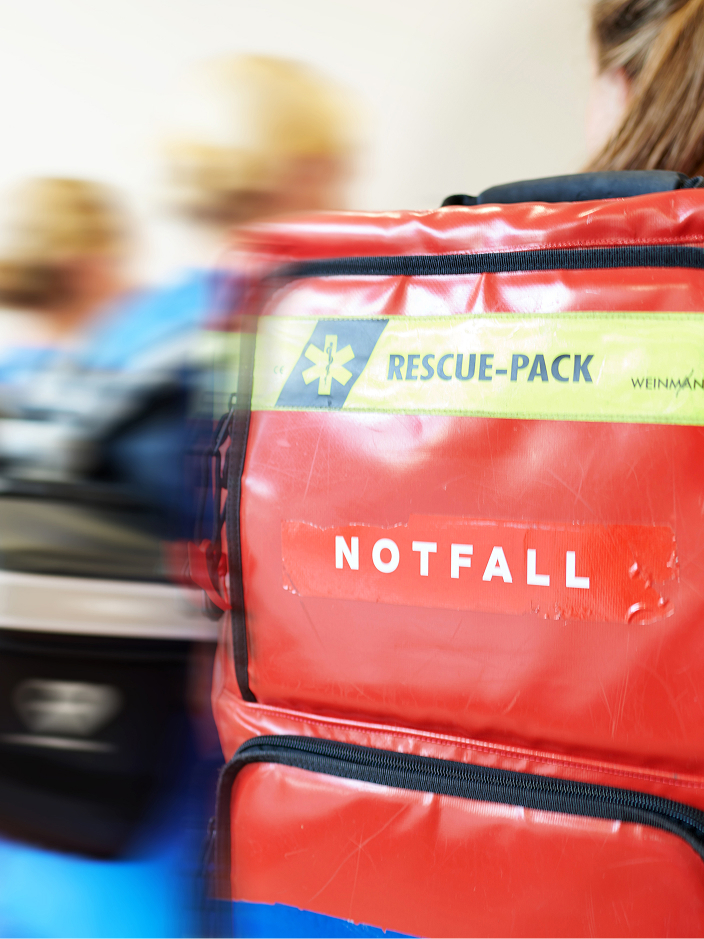 Eine Sanitäterin trägt eine rote Notfalltasche mit der Aufschrift