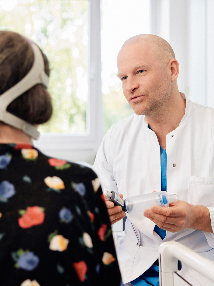 Ein Arzt spricht mit einer Patientin, während er ein medizinisches Gerät hält.