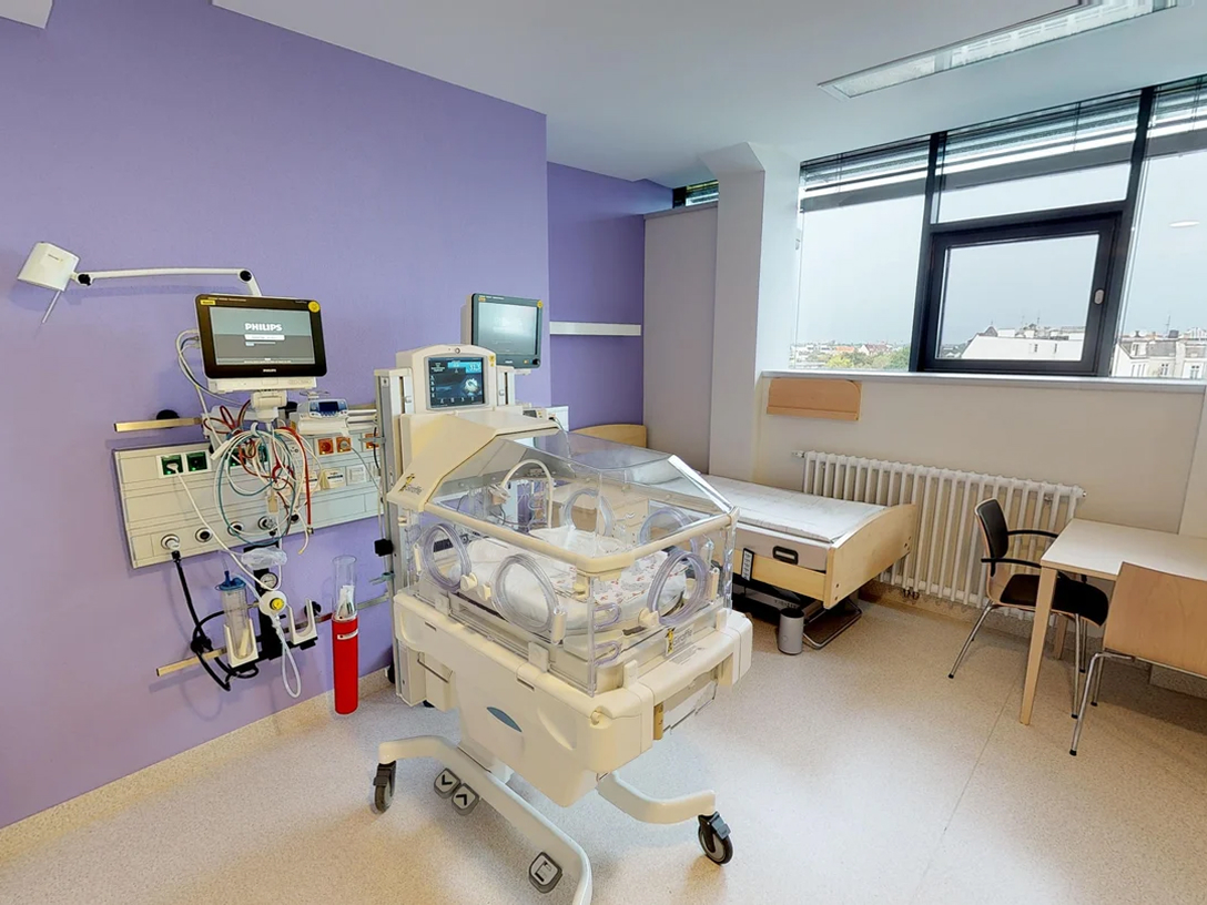 Neonatale Intensivstation mit Inkubator, Monitoren und einem leeren Bett in einem hellen, modernen Raum.