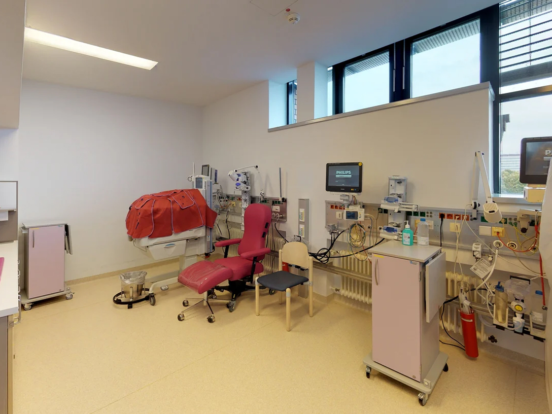 Moderner Behandlungsraum mit einem roten Stuhl, medizinischen Geräten und Monitoren.