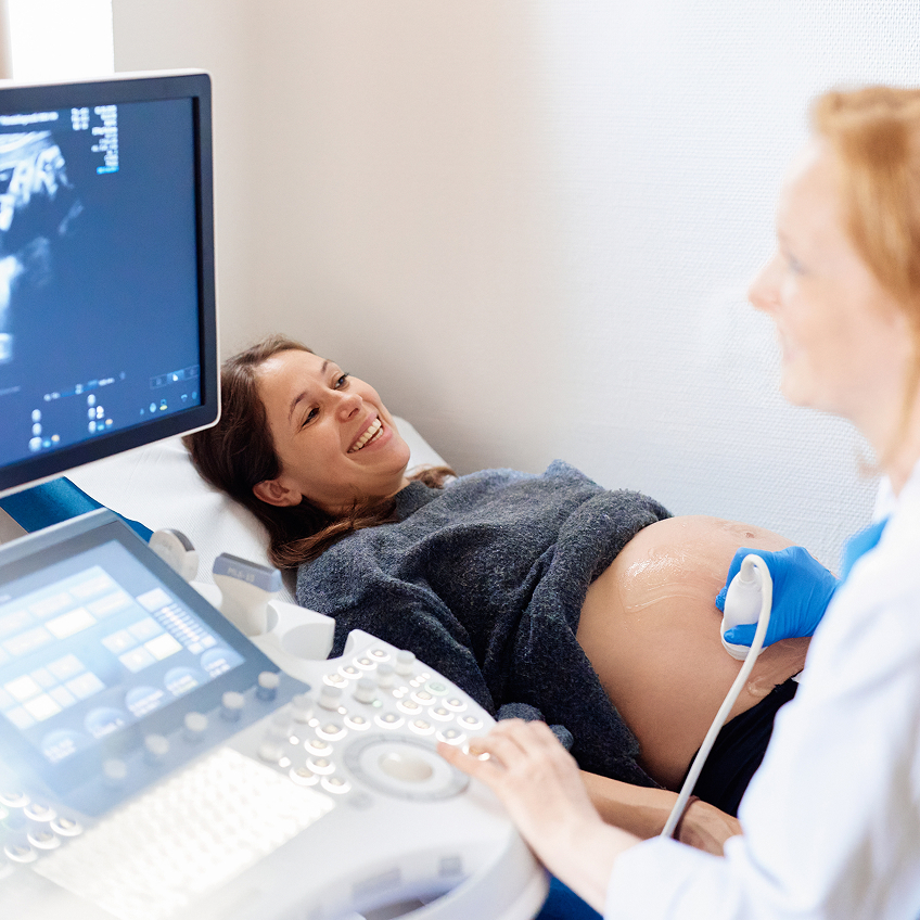 Schwangere Frau lächelt während einer Ultraschalluntersuchung, die von einer Ärztin durchgeführt wird.