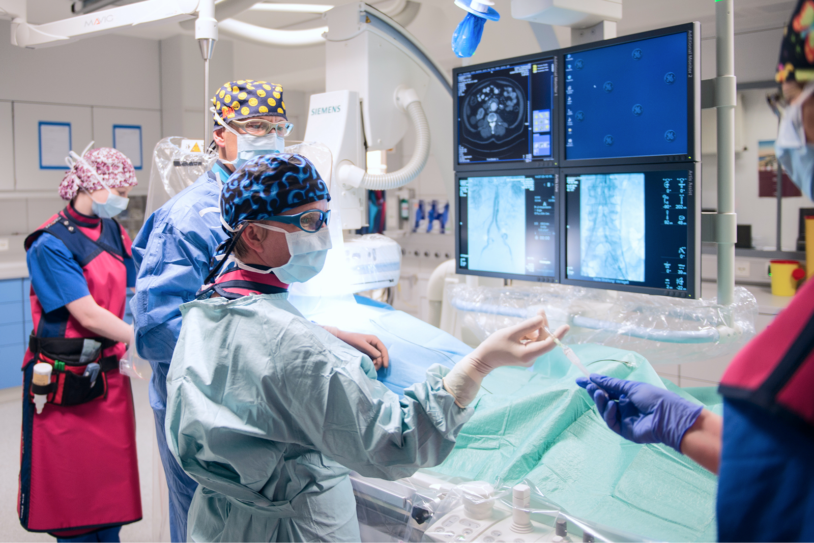 Medizinisches Team in einem Operationssaal, das an einem Patienten arbeitet, während Bildschirme mit medizinischen Daten angezeigt werden.
