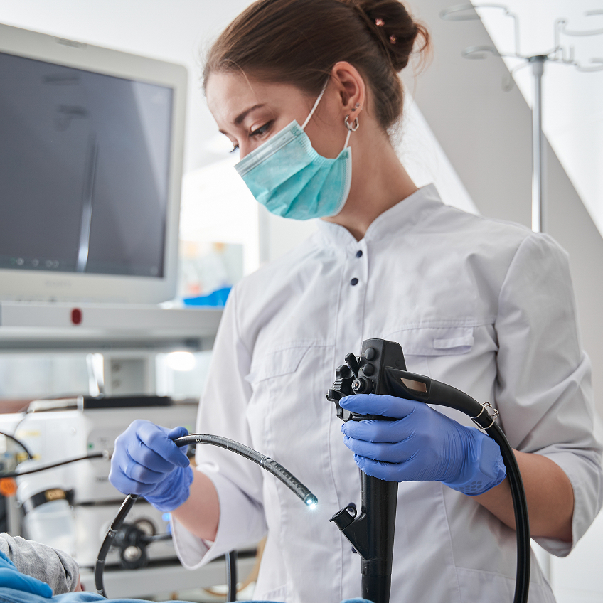 Eine medizinische Fachkraft in Schutzkleidung führt einen Eingriff mit einem Endoskop an einem Patienten durch.