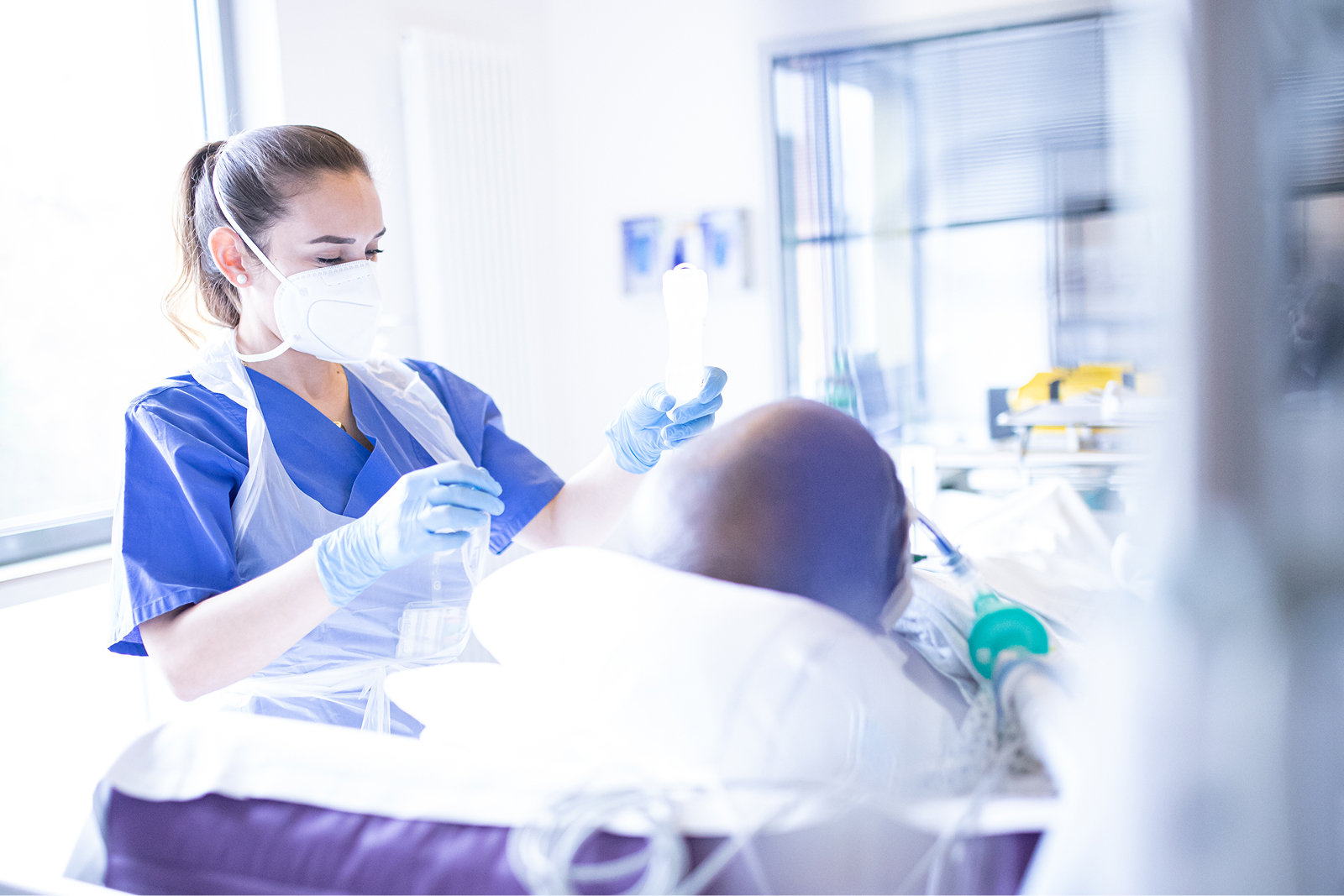Eine medizinische Fachkraft mit blauer Arbeitskleidung und Mundschutz kümmert sich um einen Patienten.