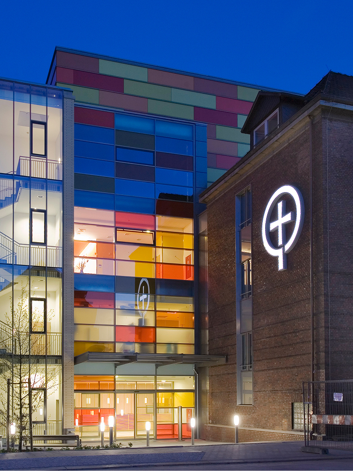 Moderner, gläserner Anbau an ein historisches Gebäude, beleuchtet bei Nacht.