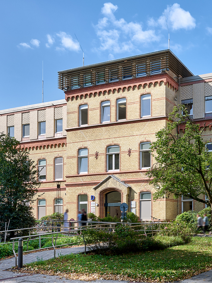 Historisches Gebäude mit gelber Fassade, umgeben von Bäumen und einem gepflegten Garten.