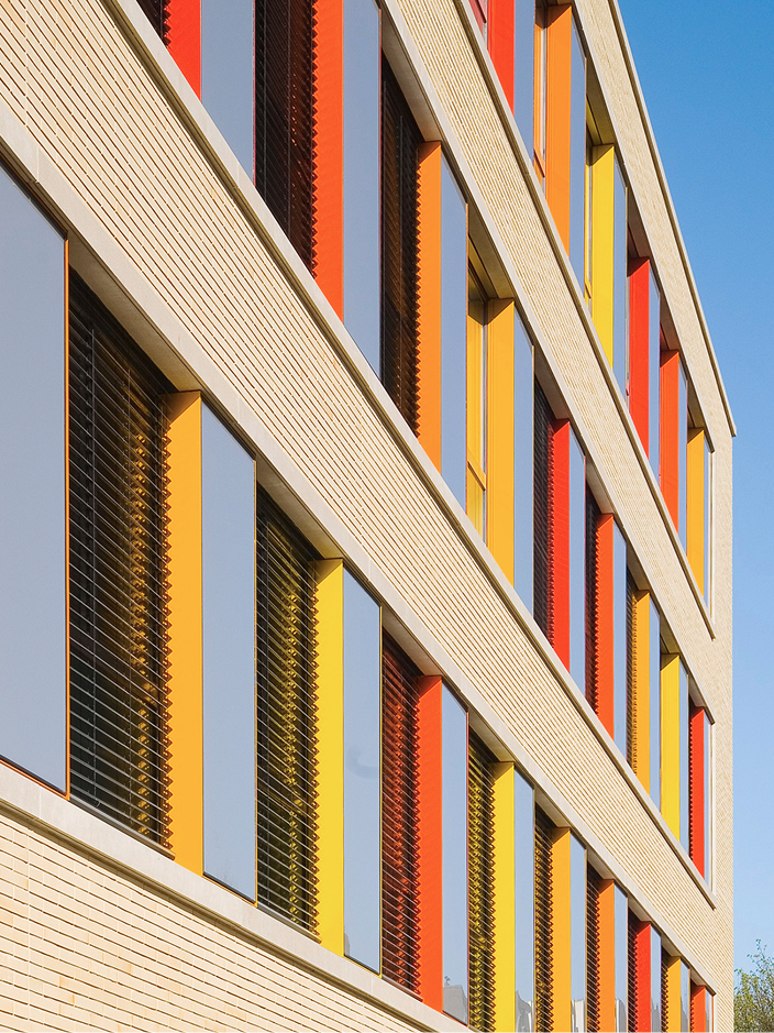 Fassade eines Gebäudes mit bunten Fenstern in Rot, Gelb und Orange vor einem blauen Himmel.