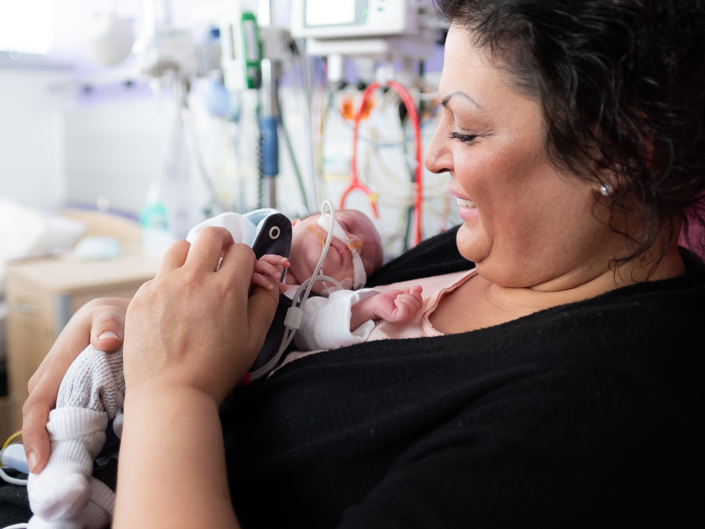 Eine Frau hat ein neugeborenes Baby auf ihrer Brust, sie schaut es liebevoll an und lächelt.