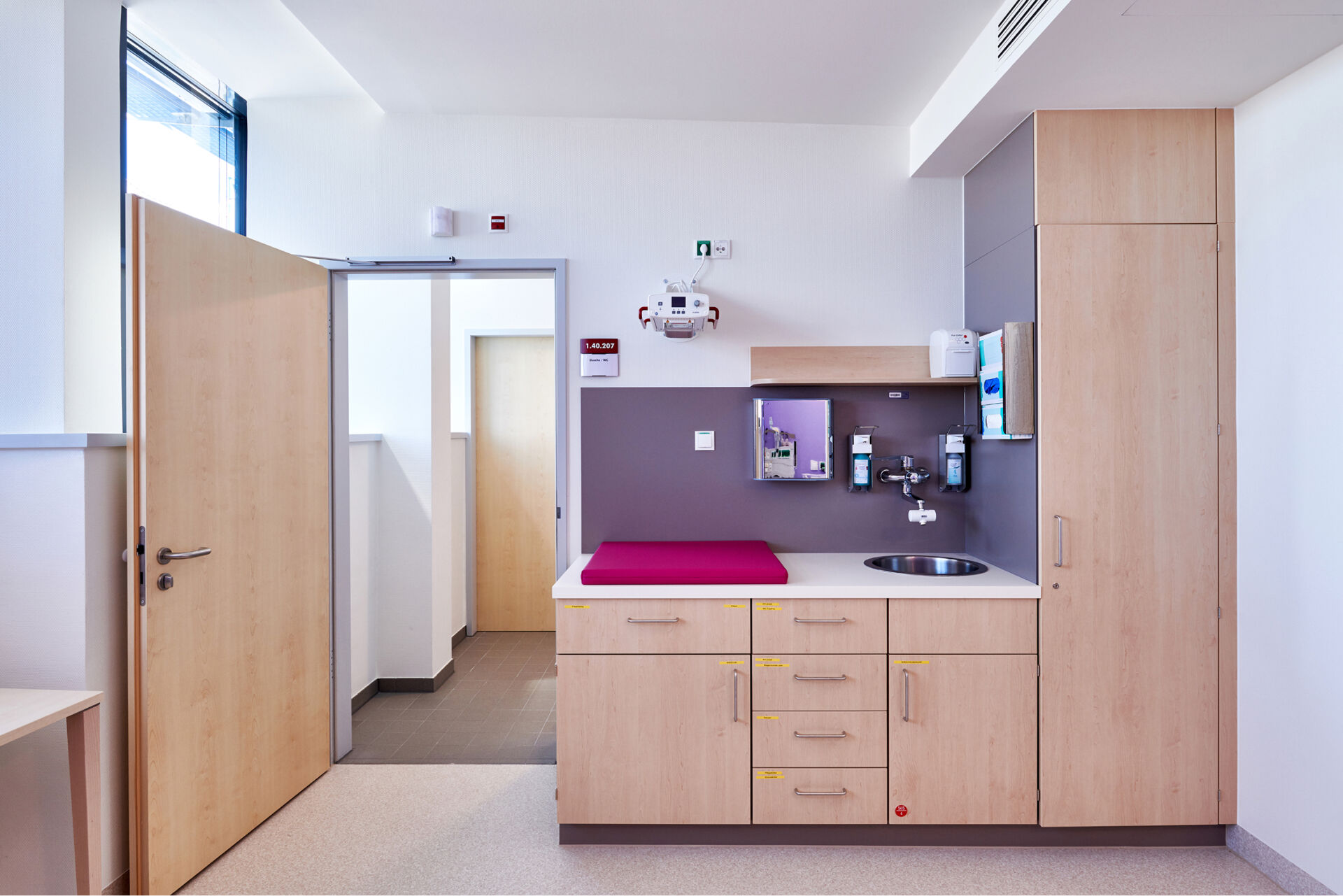 Moderne, helle Schrankwand, Wickeltisch und Waschbecken neben einer offenen Tür.