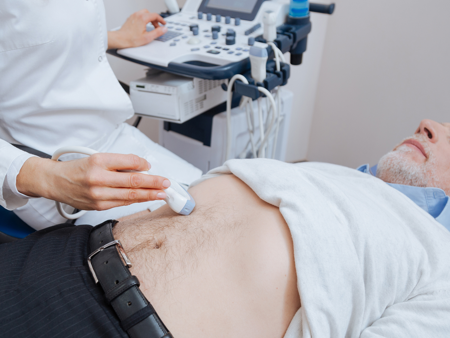 Ein Arzt führt einen Ultraschall am Bauch eines Patienten durch, im Hintergrund ist das Ultraschallgerät sichtbar.