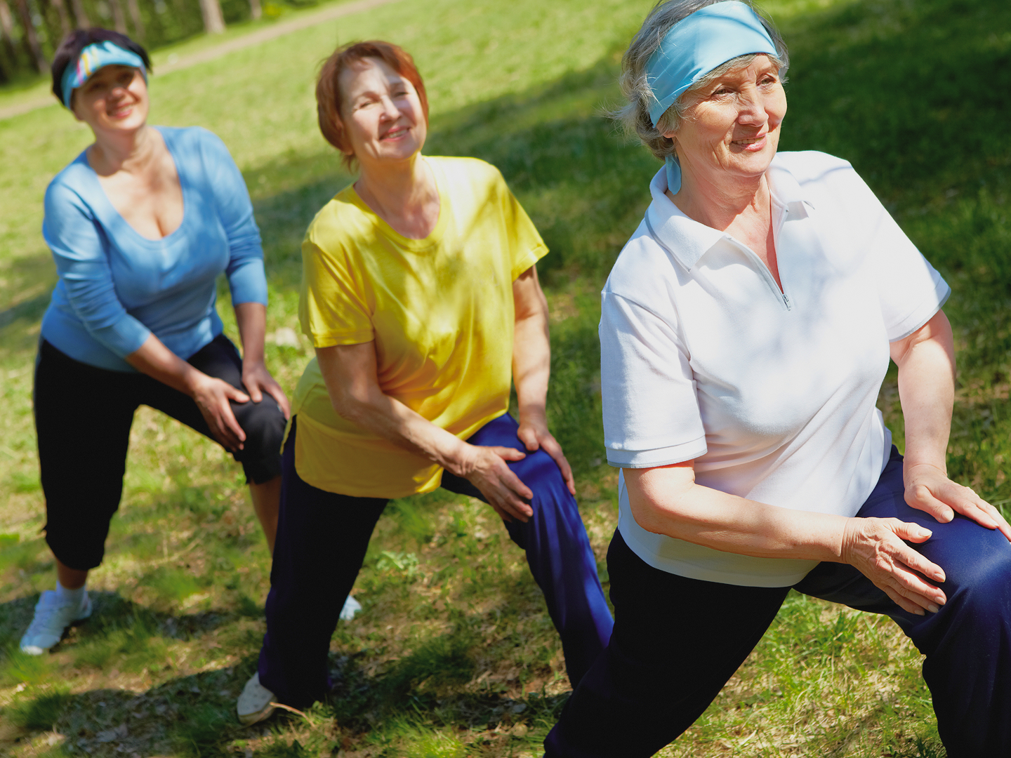 Drei Frauen in Sportkleidung dehnen sich im Freien auf einer Wiese.