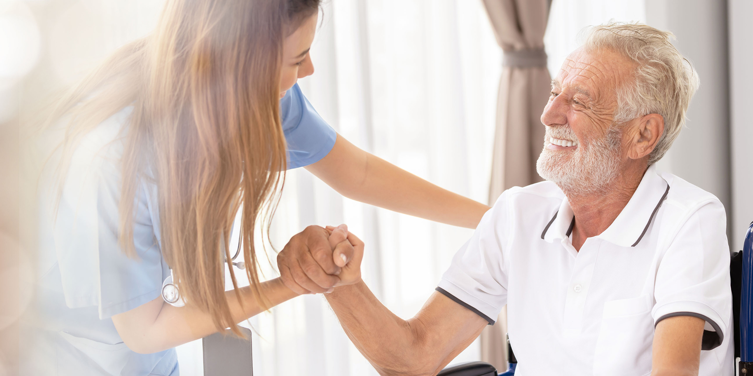 Eine Pflegekraft hält die Hand eines lächelnden älteren Mannes, während sie sich freundlich unterhalten.