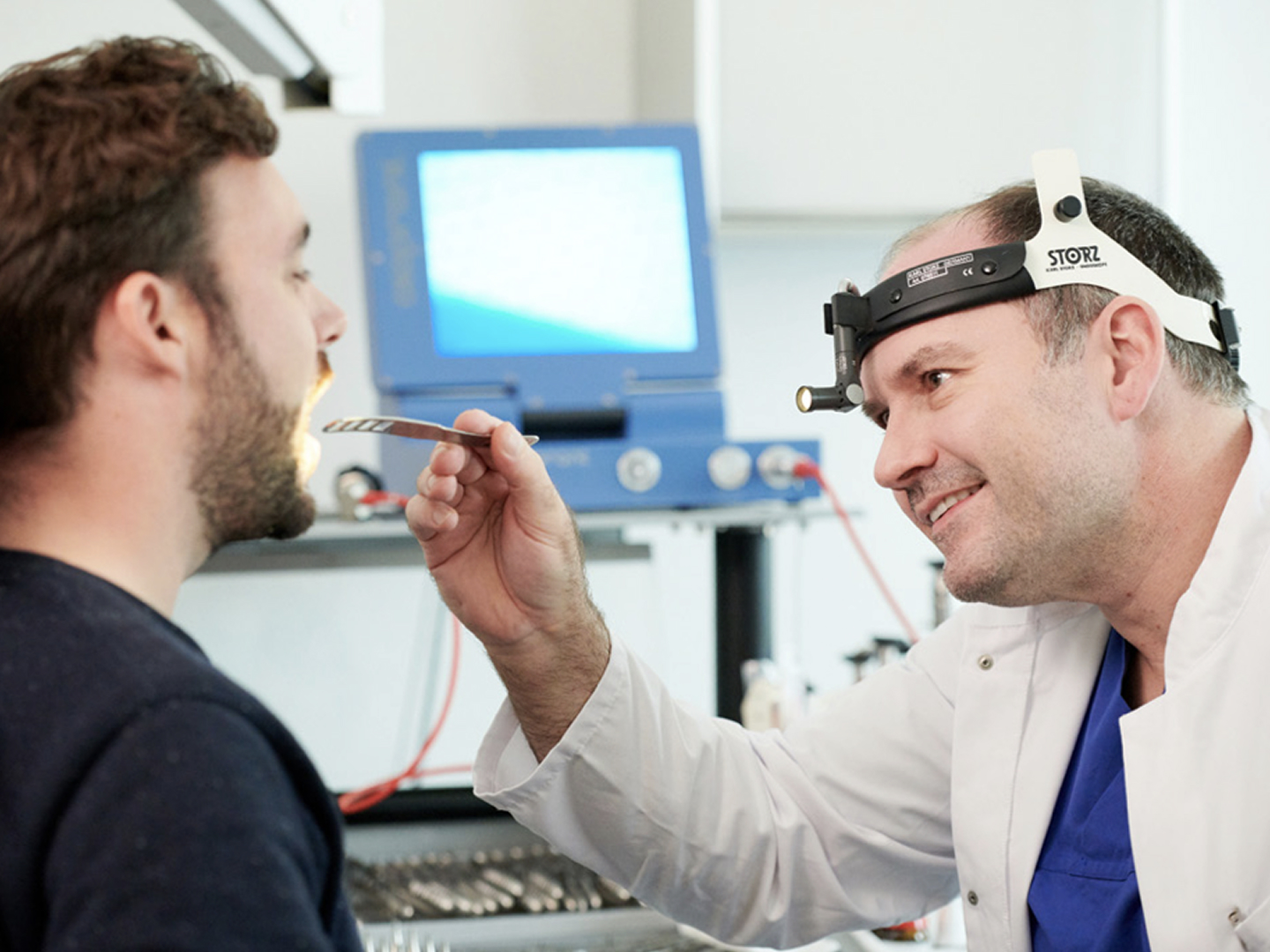 Ein Arzt untersucht den Mund eines Patienten mit einem Instrument in einer modernen medizinischen Umgebung.