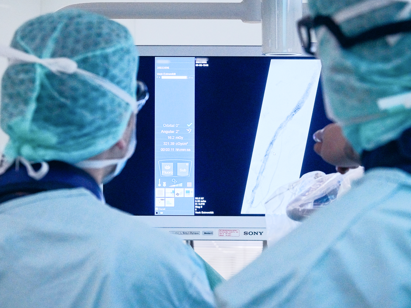 Zwei Chirurgen in OP-Kleidung betrachten einen Monitor mit medizinischen Bildern.