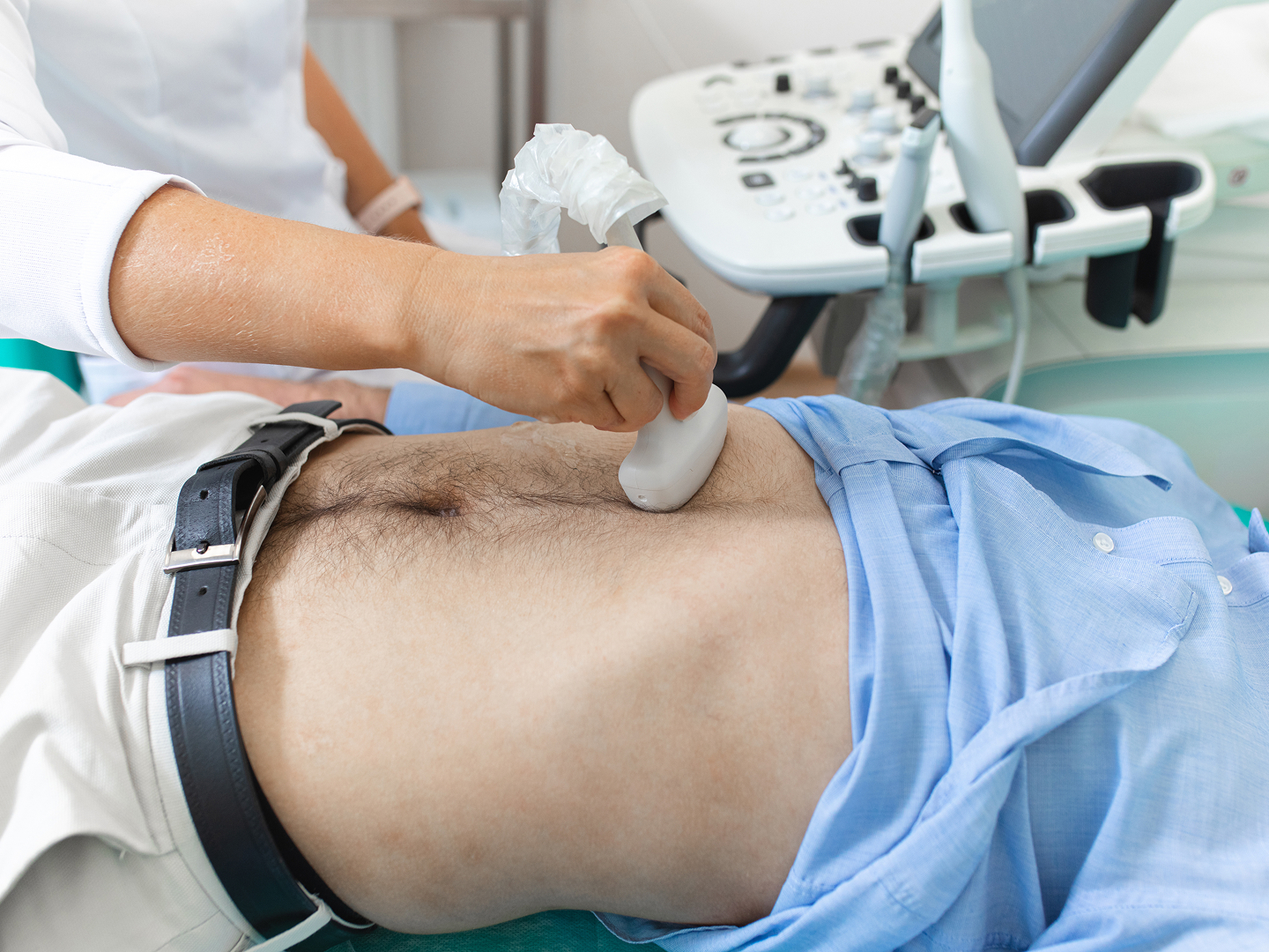 Ein Arzt führt einen Ultraschall am Bauch eines Patienten durch, der auf einer Liege liegt.