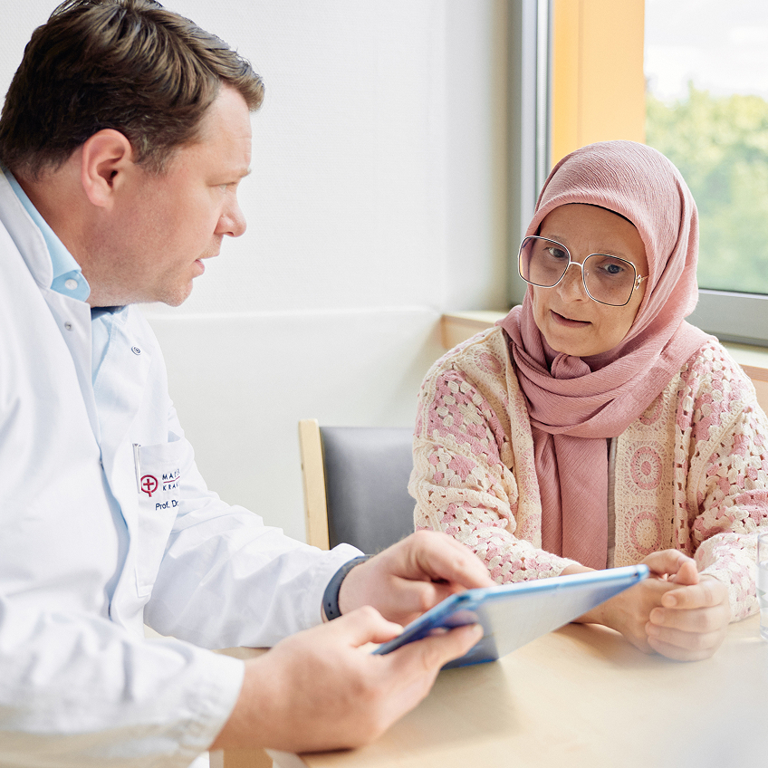 Ein Arzt und eine Patientin im Gespräch, während sie auf ein Tablet schaut, dass der Arzt in der Hand hält.