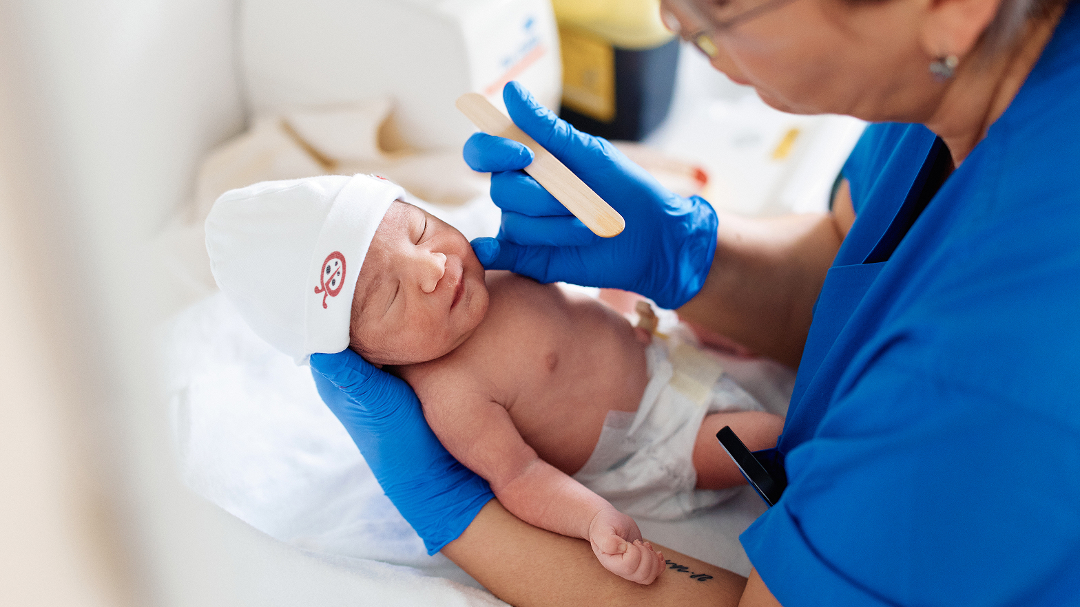 Ein Neugeborenes wird von einer Person mit blauen Handschuhen untersucht.