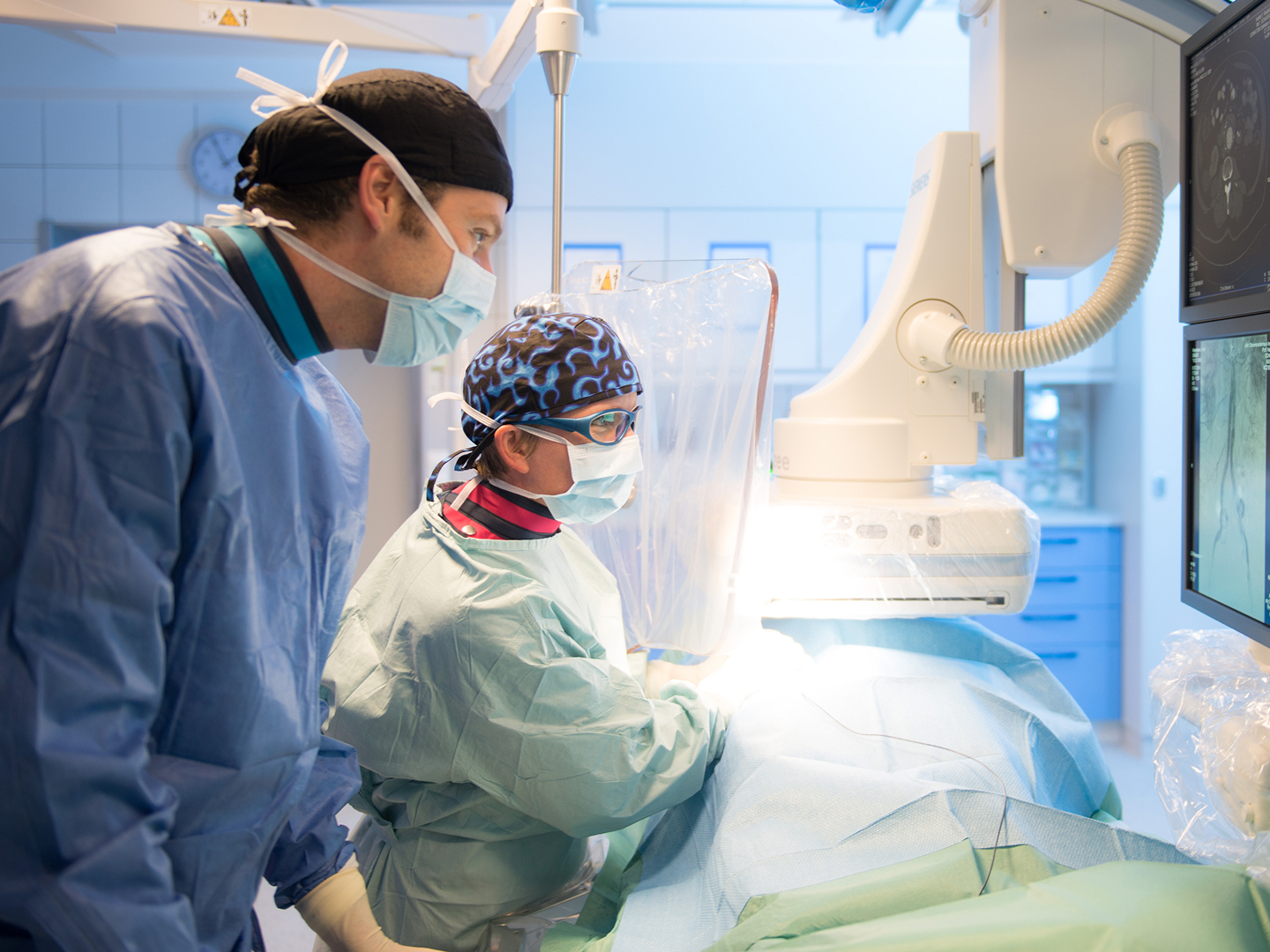 Zwei Chirurgen in OP-Kleidung arbeiten konzentriert an einem Patienten, umgeben von medizinischen Geräten.