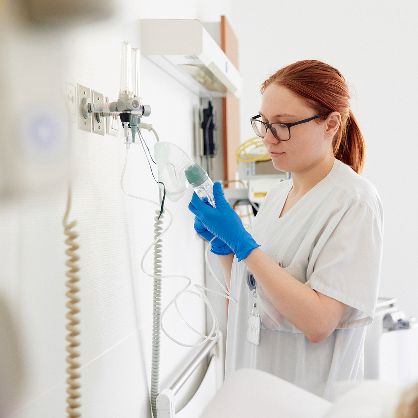 Eine Krankenschwester in blauen Handschuhen überprüft eine Infusionsleitung in einem Krankenhauszimmer.