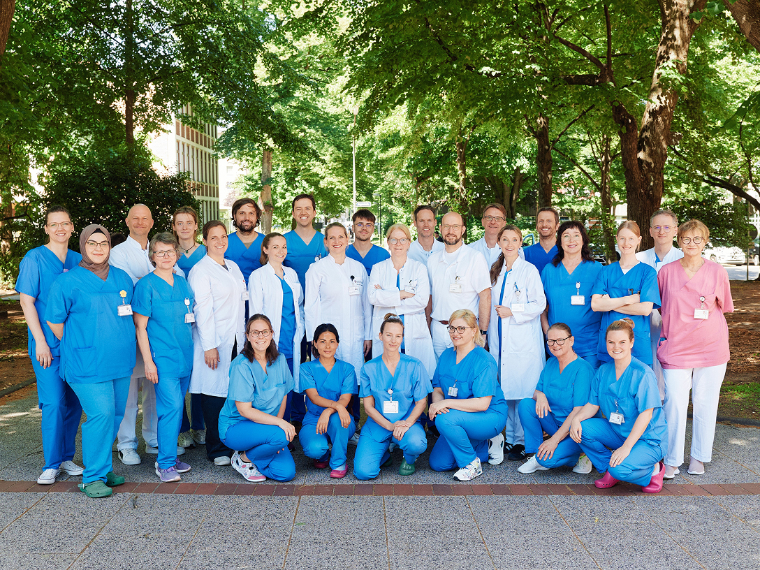 Gruppe von Personen in medizinischer Kleidung, die im Freien vor Bäumen posiert.