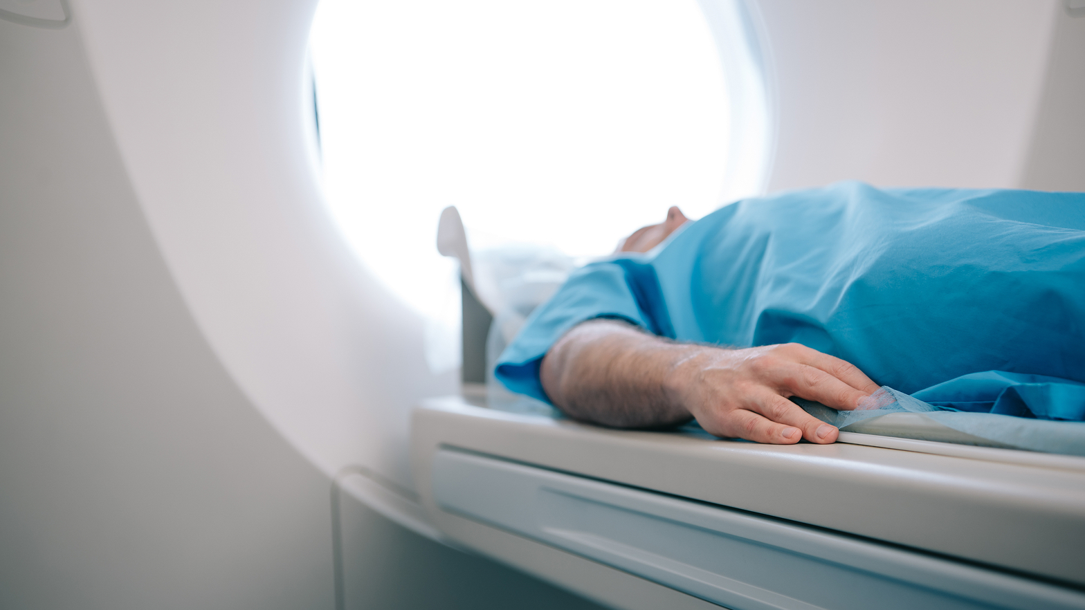 Ein Patient in blauem Krankenhaushemd liegt für eine Herzbildgebung auf der Liege eines Scanners.