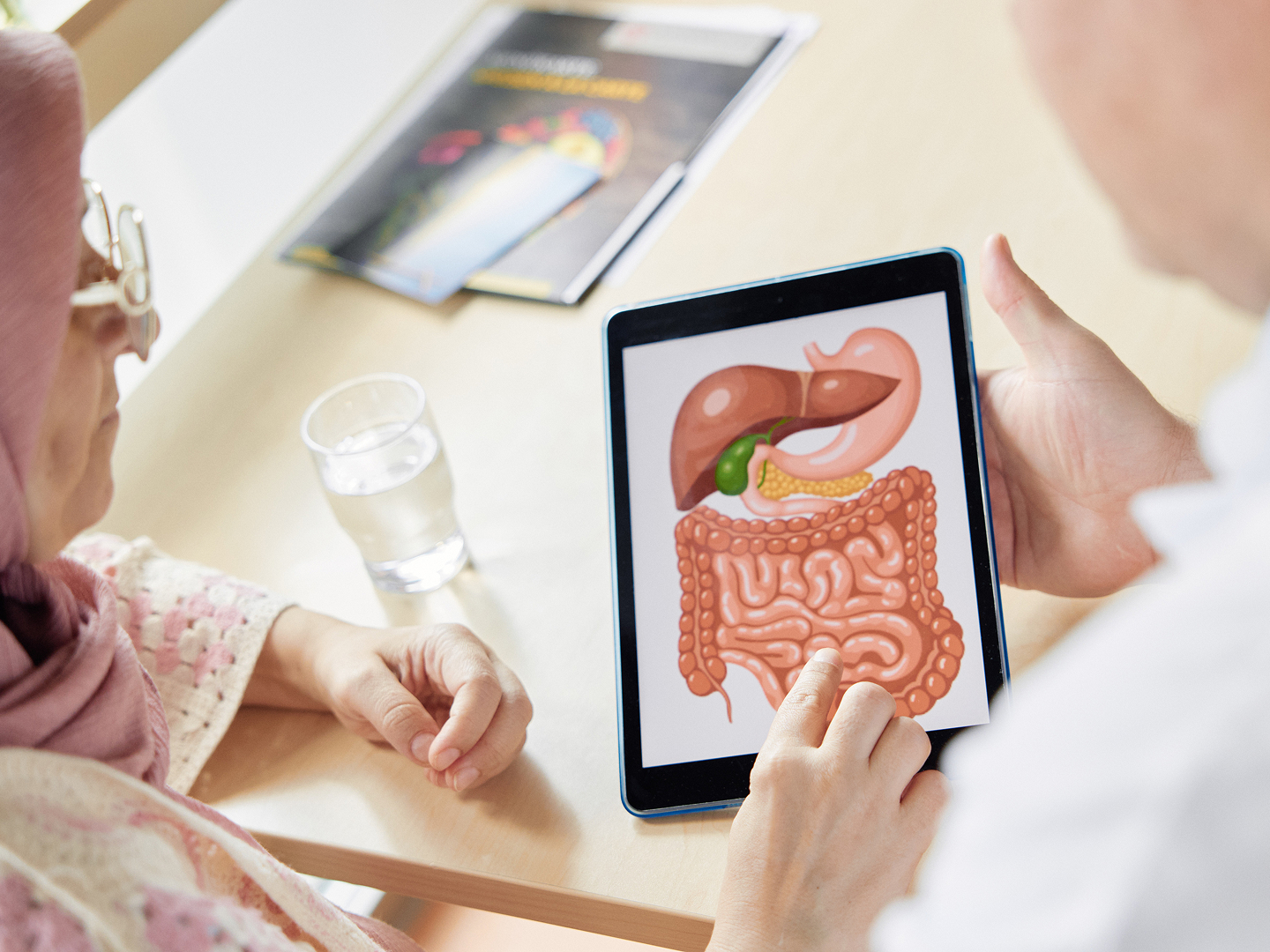 Ein Arzt zeigt einer älteren Frau auf einem Tablet eine anatomische Darstellung des Verdauungssystems.