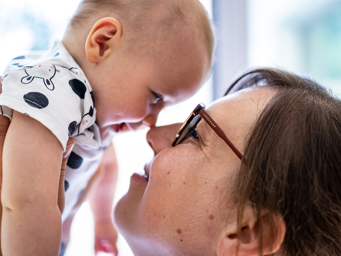 Ein Baby und eine Frau lächeln sich an, ihre Nasen berühren sich.