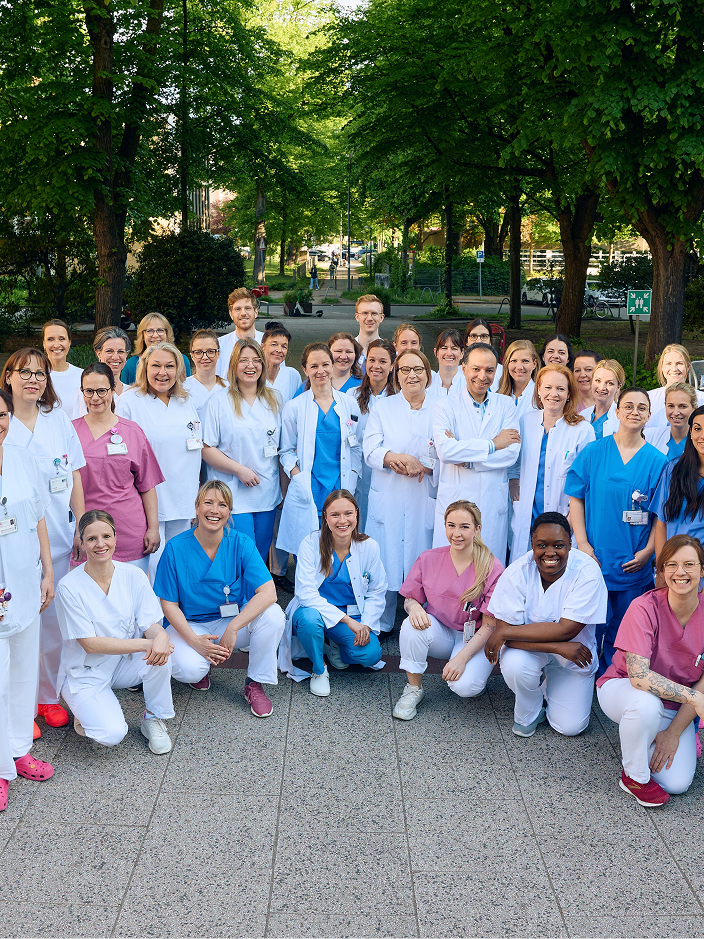 Eine Gruppe von mehreren medizinischen Fachkräften in Arbeitskleidung steht im Freien und posiert für ein Foto.