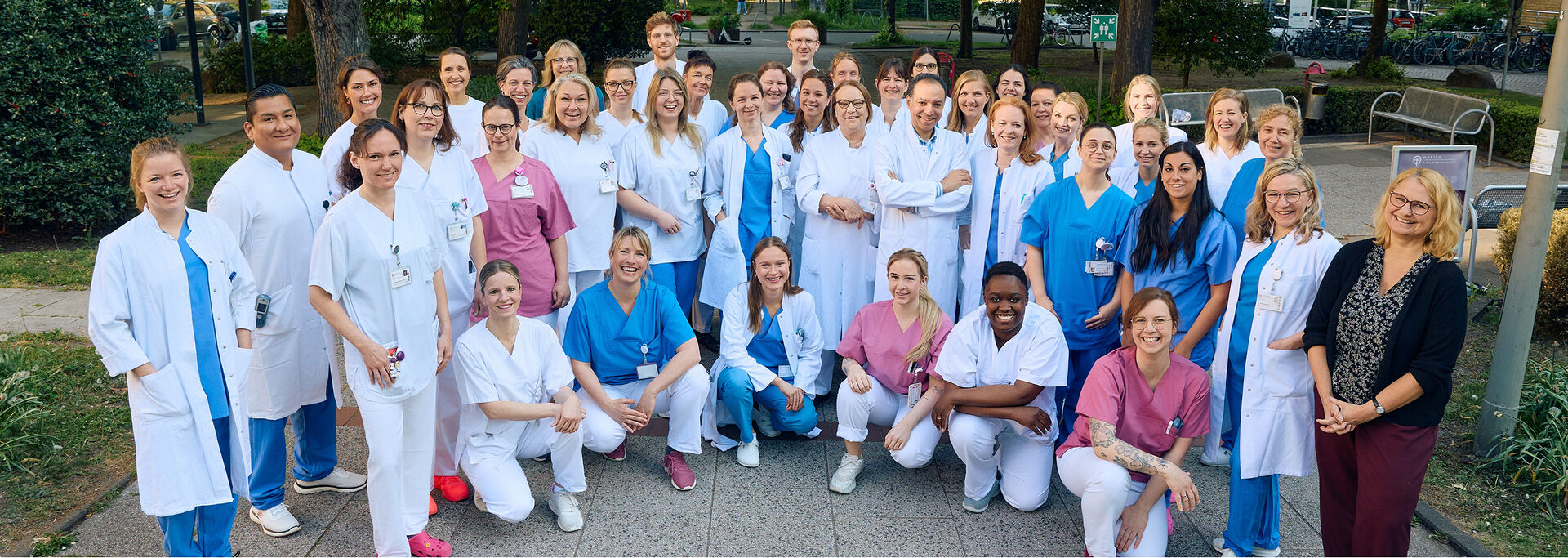 Eine Gruppe von mehreren medizinischen Fachkräften in Arbeitskleidung steht im Freien und posiert für ein Foto.