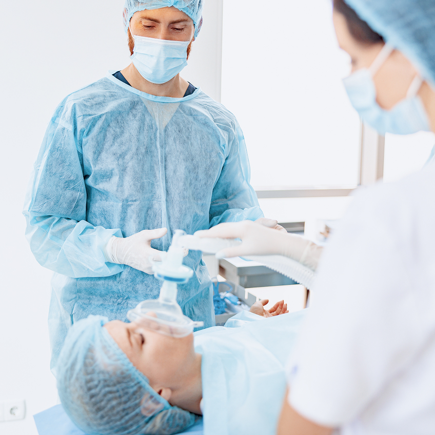Zwei medizinische Fachkräfte in Schutzkleidung behandeln einen Patienten, der auf einem Behandlungstisch liegt.