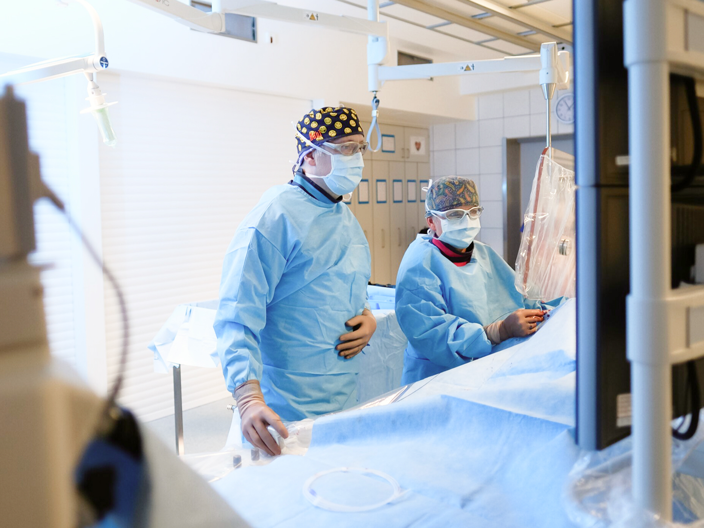 Zwei medizinische Fachkräfte in blauen OP-Kitteln und Masken arbeiten in einem hellen, modernen Behandlungsraum.