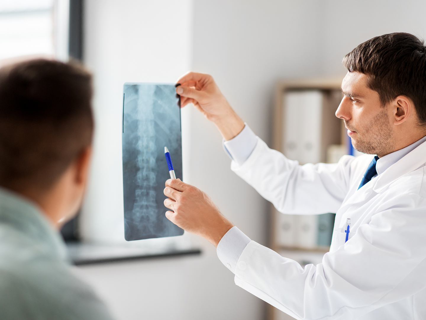 Ein Arzt zeigt einem Patienten ein Röntgenbild und weist mit einem Stift auf Details hin.