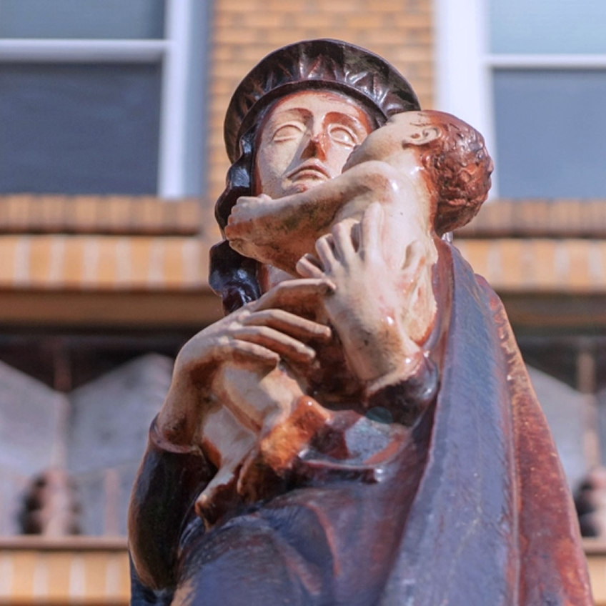 Eine Statue einer Frau vor einem Gebäude mit Fenstern, die ein Kind in den Armen hält.