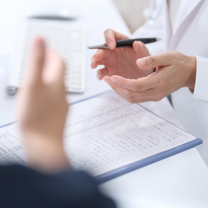 Hände eines Arztes und eines Patienten während eines Gesprächs über medizinischen Unterlagen.