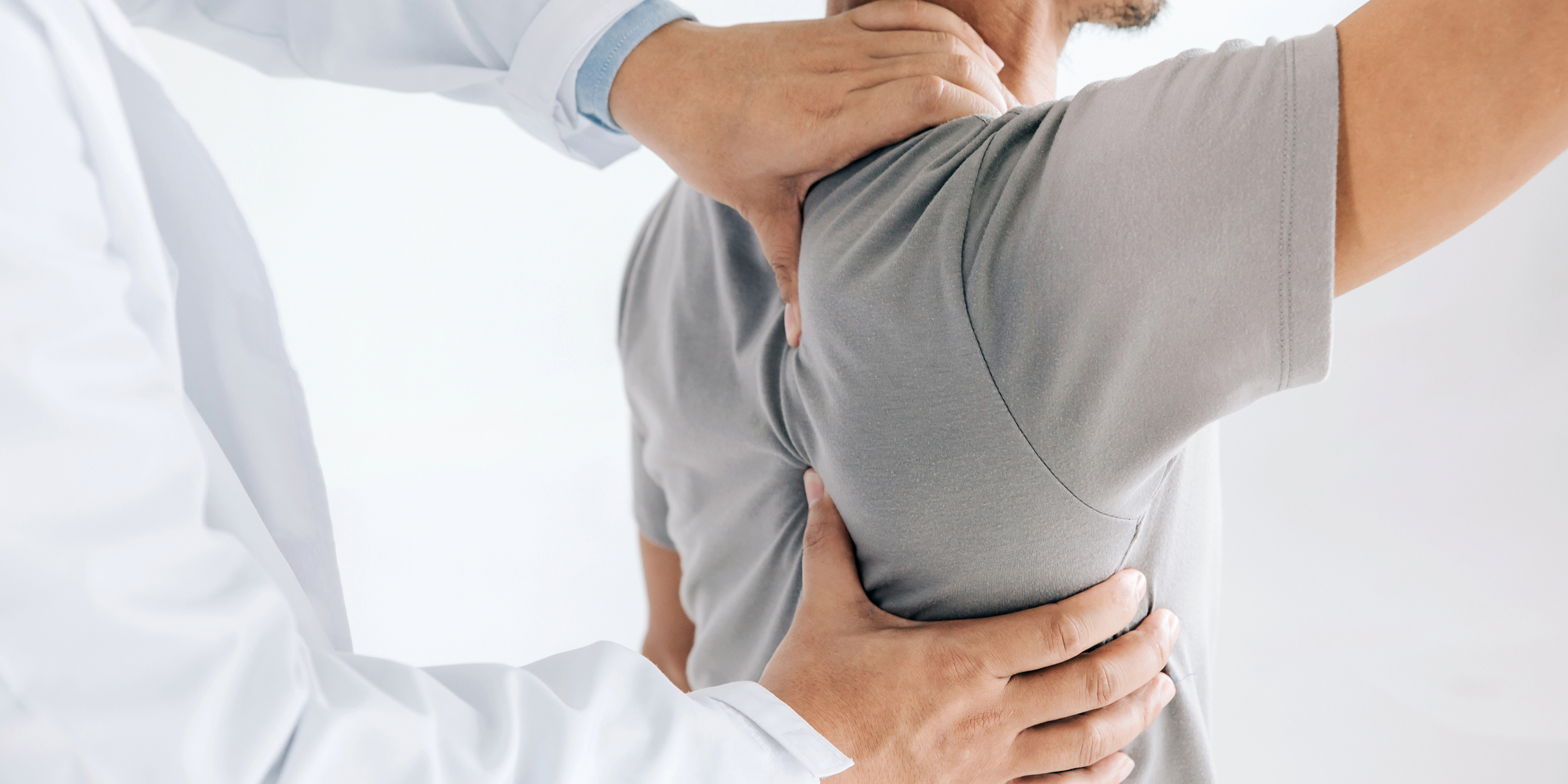 Ein Arzt untersucht den Nacken und die Schulter eines Patienten.