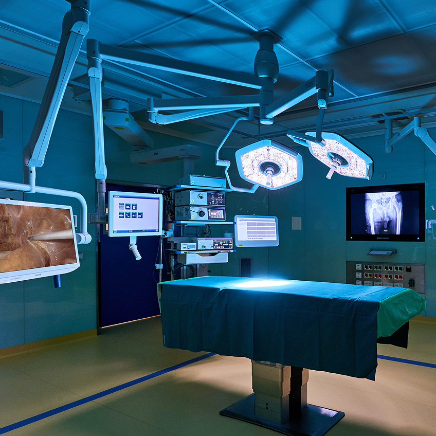 Operationssaal mit einem chirurgischen Tisch, medizinischen Geräten und OP-Lichtern in blauer Beleuchtung.