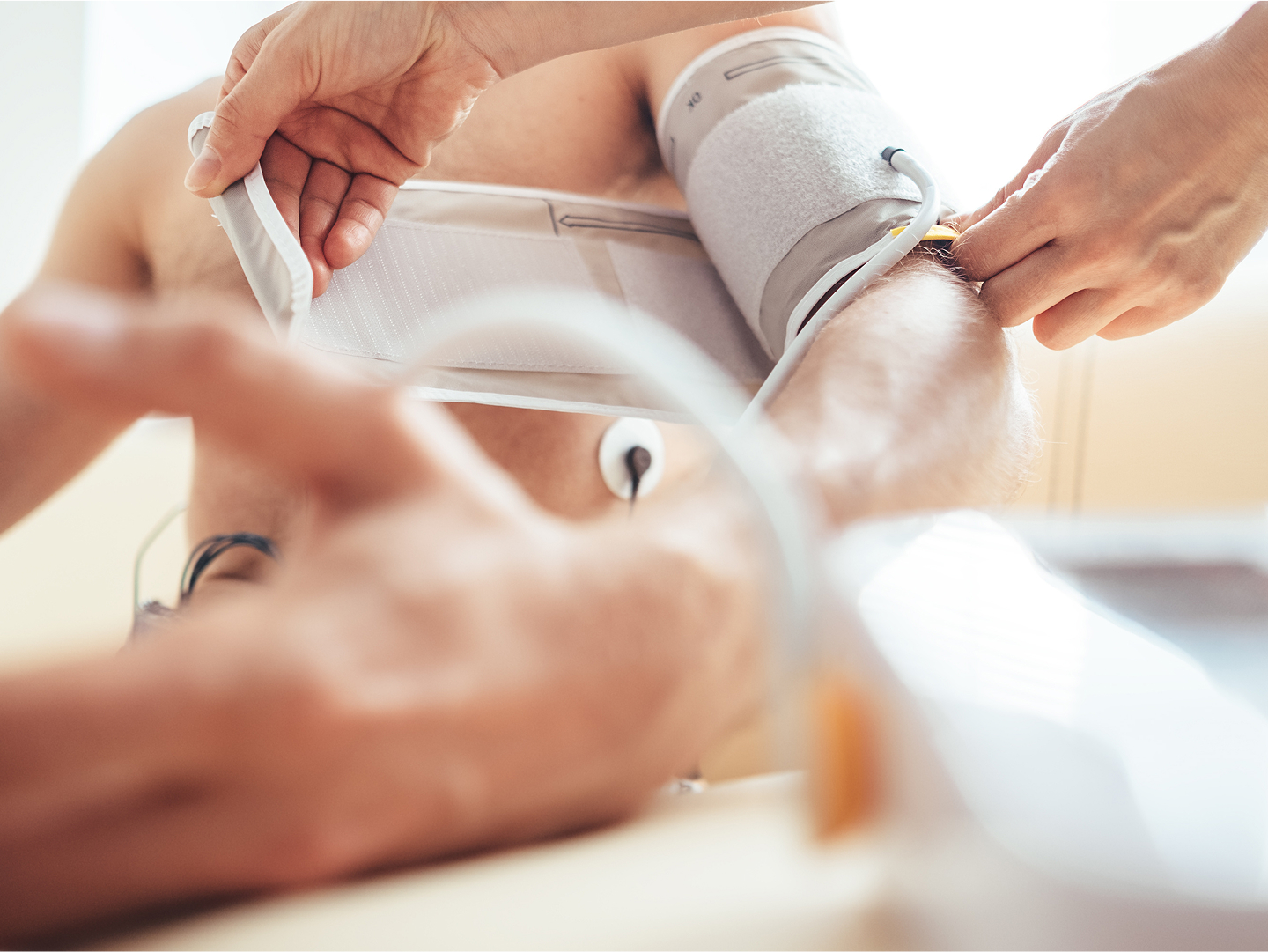 Eine Person erhält eine Blutdruckmessung am Arm, man sieht die Hände der medizinischen Fachkraft.