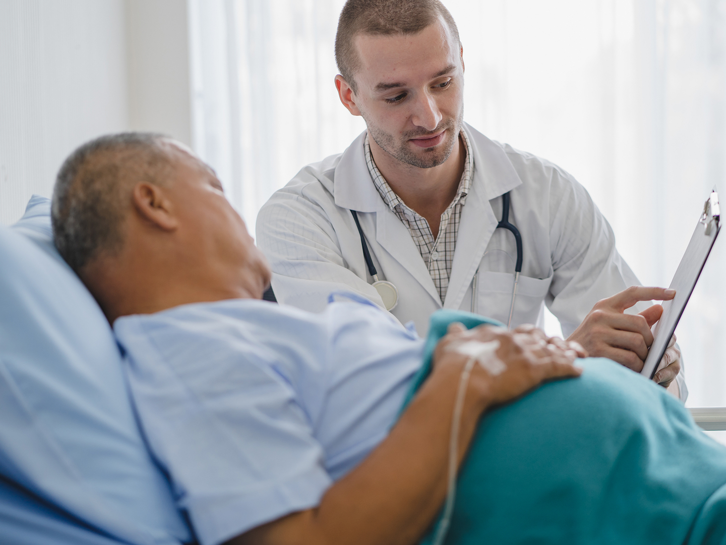 Ein Arzt spricht mit einem Patienten im Bett, während er eine medizinische Untersuchung durchführt.