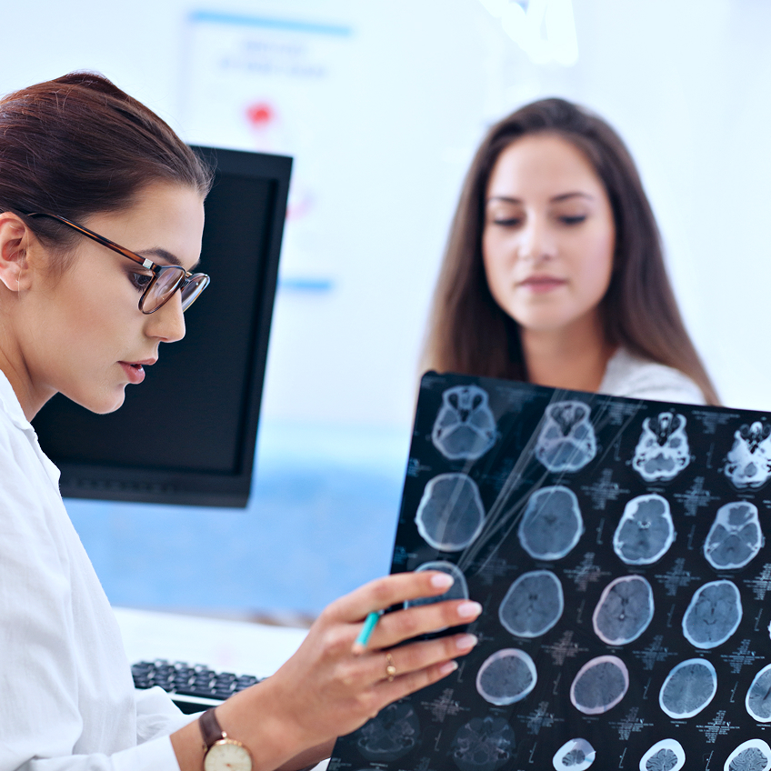 Ärztin zeigt einer Patientin die Aufnahmen ihres Schädels in einem modernen Behandlungsraum.