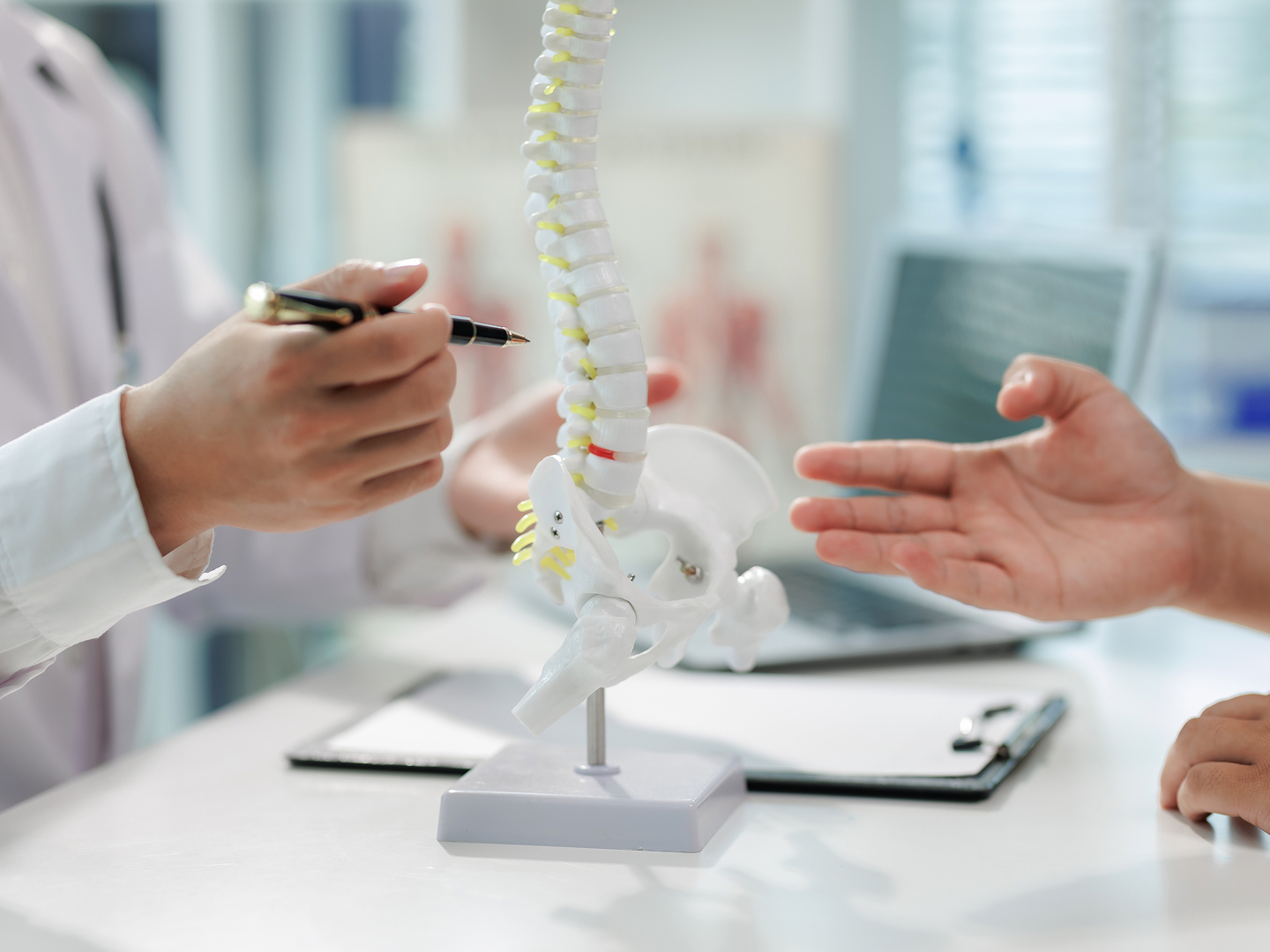 Ein Arzt berät einen Patienten, während er mit einem Stift auf ein Wirbelsäulenmodell zeigt.
