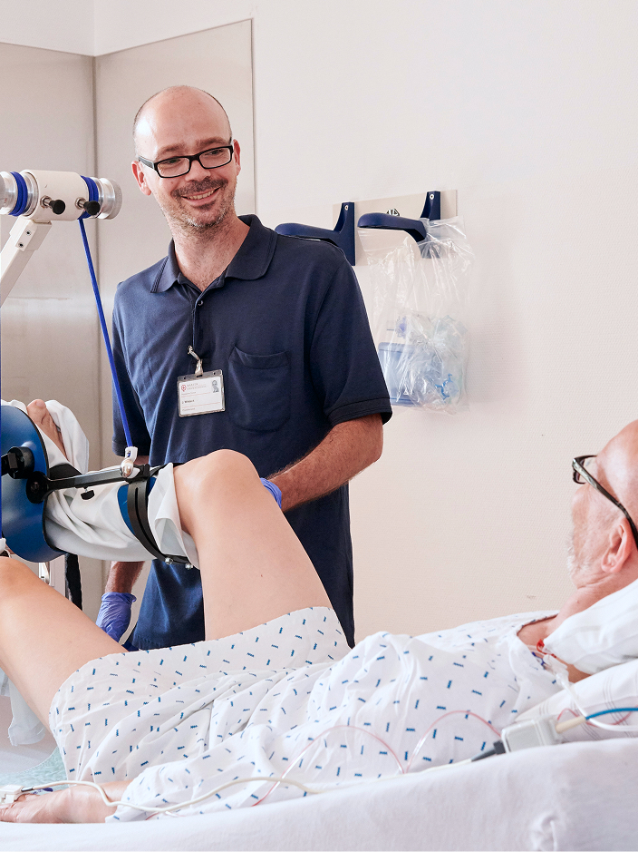 Ein Physiotherapeut hilft einem Patienten, dessen Bein während einer Behandlung in einer Schiene steckt.